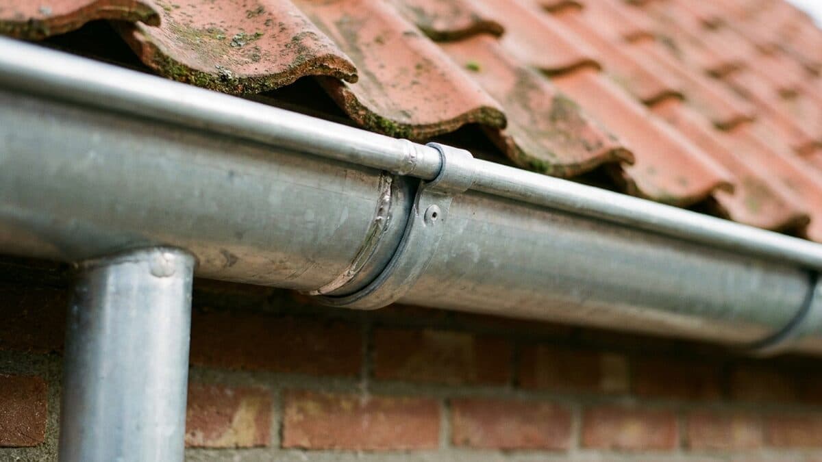 Nieuwe zinken dakgoot langs de dakvoet van een woning met rode pannen